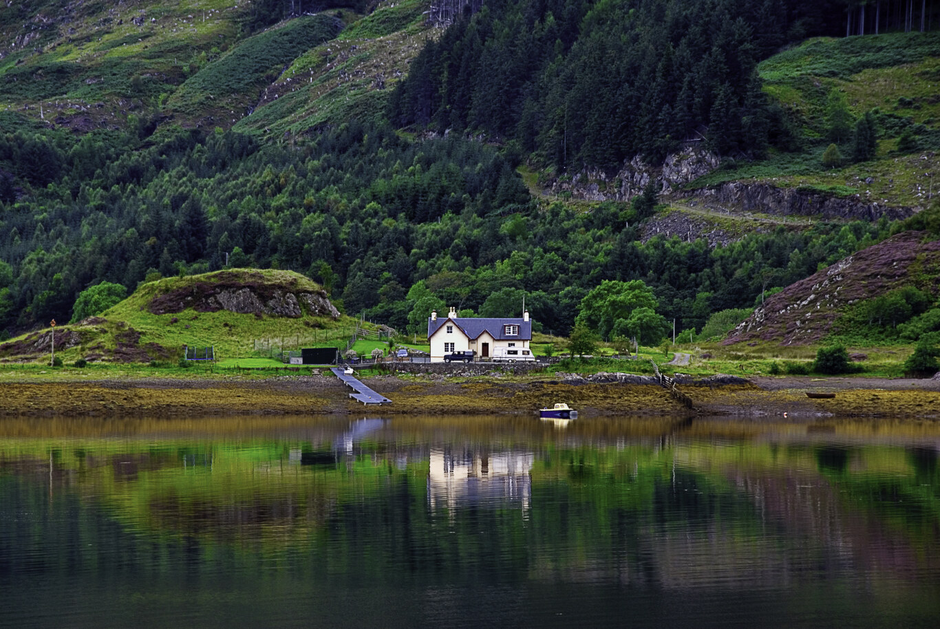 Scottish loch with white boathouse reflected in still water